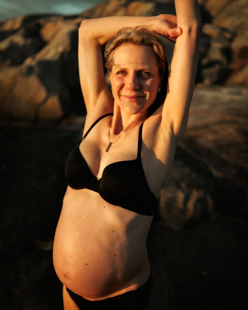 Gravid kvinna vid klipporna i Göteborg i solnedgången.