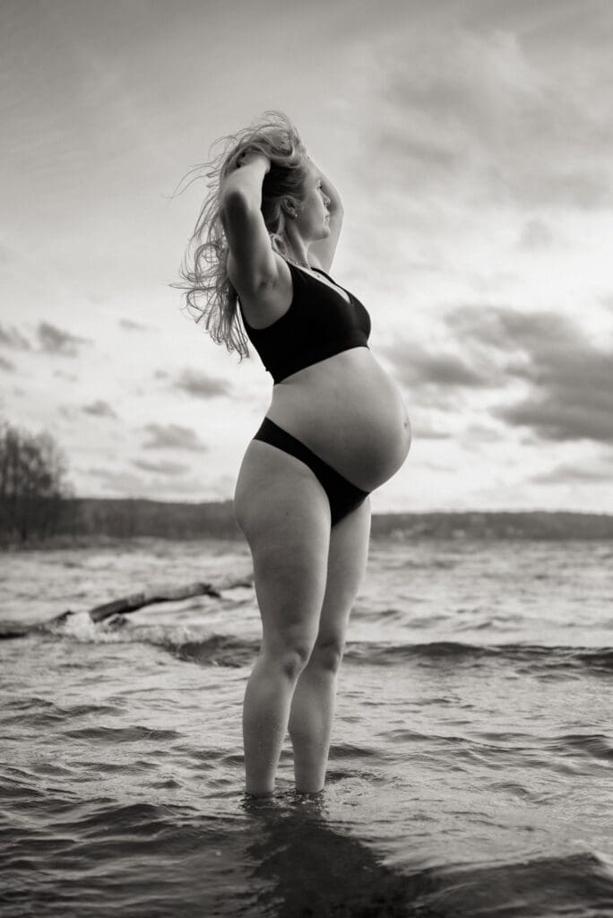 Gravid kvinna står i vattnet i Aspen i Lerum med händerna i håret och blickar ut över sjön.