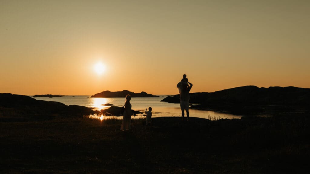 Familj som står på en klippa vid havet på Öckerö i solnedgången.