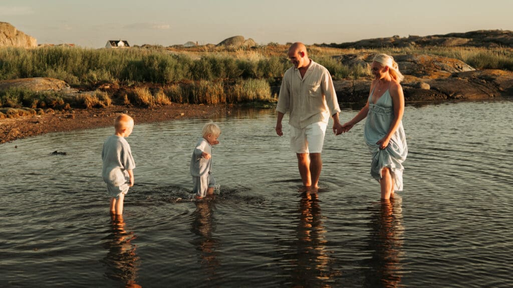 Mamma, pappa och två barn står i vattnet på Öckerö i solnedgången.
