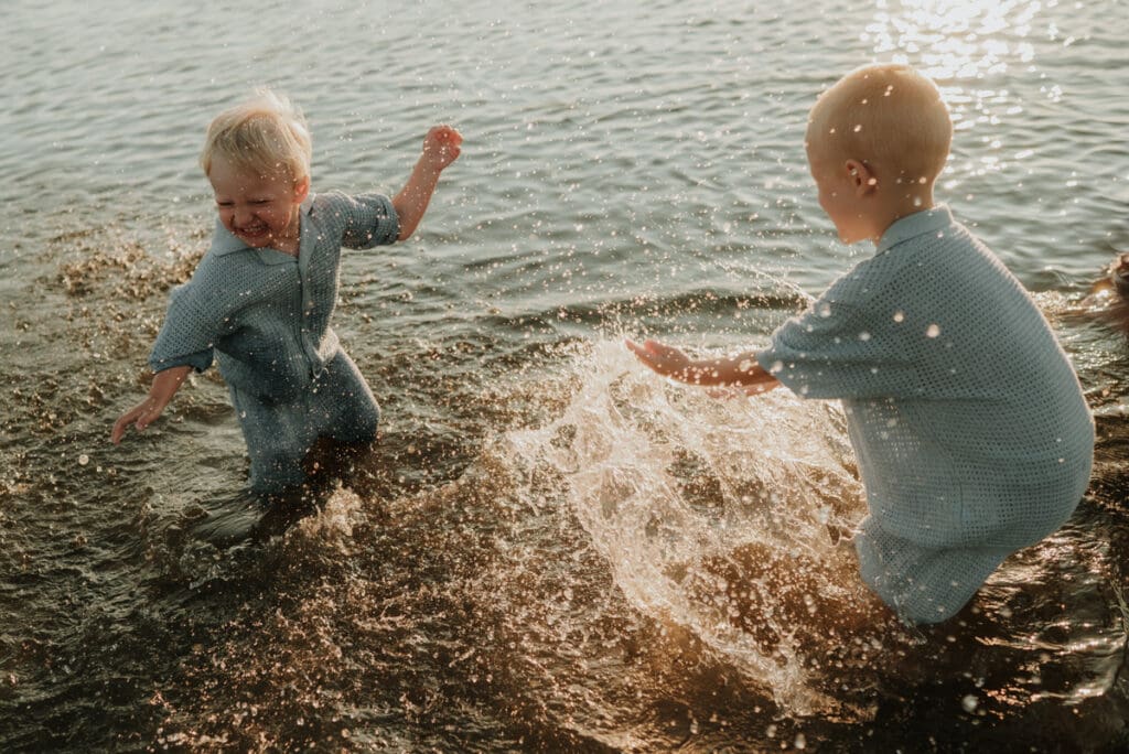 Två yngre barn står i havet på Öckerö och skvätter vatten på varandra i solnedgångsljuset.