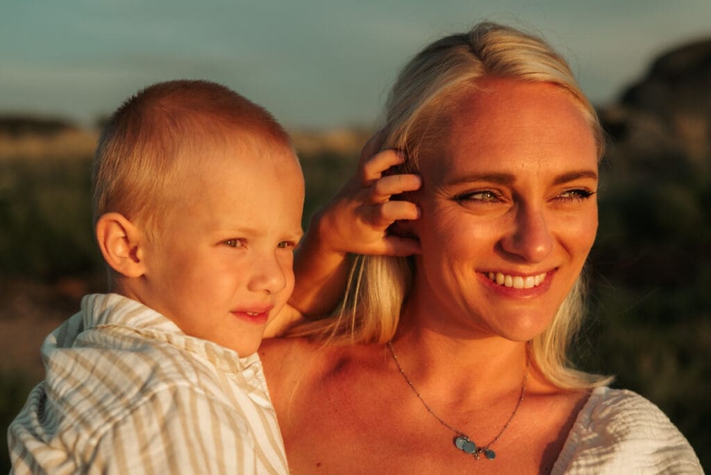 En pojke i sin mammas famn i golden hour vid havet på Öckerö.
